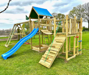 Grande aire de jeux en bois avec toboggan, mur d’escalade et pont suspendu sur une pelouse