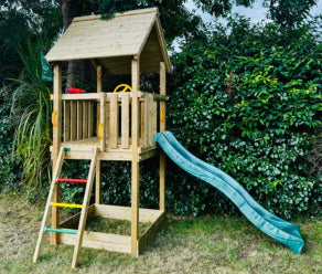Maisonnette en bois compacte avec toboggan vert et échelle d'escalade le long d'une haie